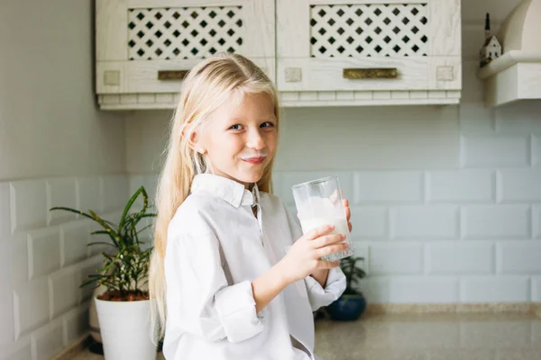 Gelukkig blond lang haar klein meisje drinken melk in de keuken, gezonde levensstijl — Stockfoto