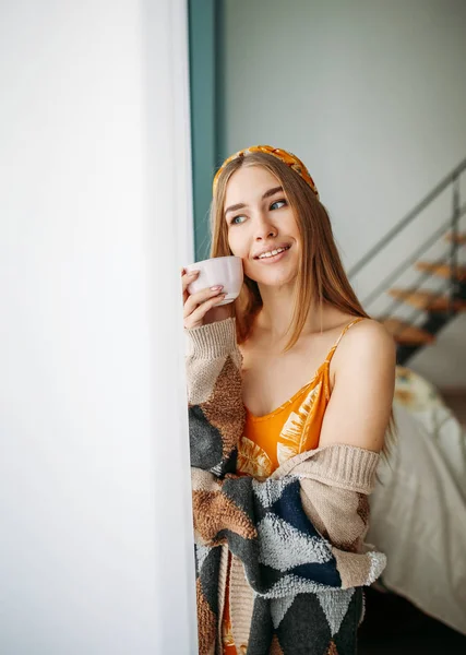 Bela sorridente jovem mulher bonita cabelo longo menina vestindo em cardigan de malha aconchegante com xícara de chá perto da janela em casa — Fotografia de Stock