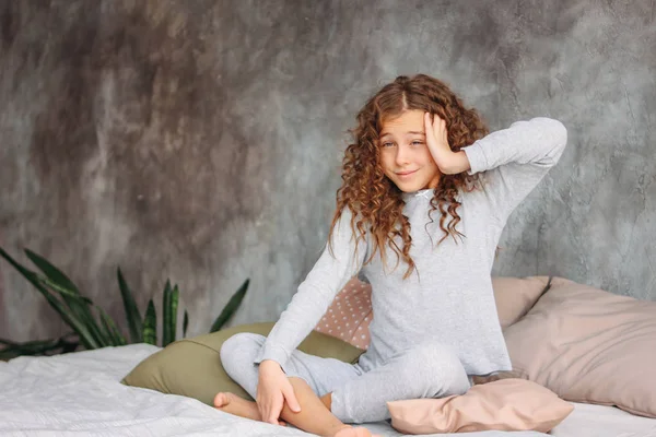 Rizado pelo hermoso adolescente chica en pijama acaba de despertar y sentado en la cama con almohada, hora de la mañana — Foto de Stock