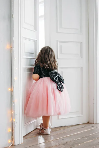 Mała dziewczynka w pięknej różowej sukience z spódnicą tutu patrzy na drzwi — Zdjęcie stockowe