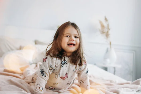 Маленькая счастливая девочка в уютной пижаме на кровати родителей в доме — стоковое фото