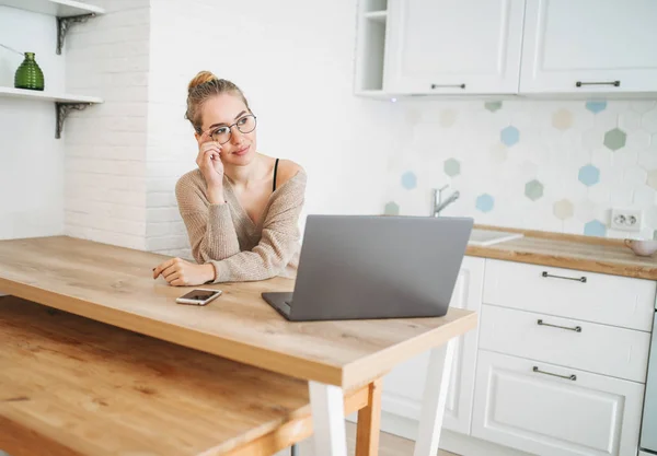 Schöne lächelnde junge Frau helles langes Haar Mädchen in Brille trägt in gemütlichen Strickpullover mit Laptop in heller Küche — Stockfoto