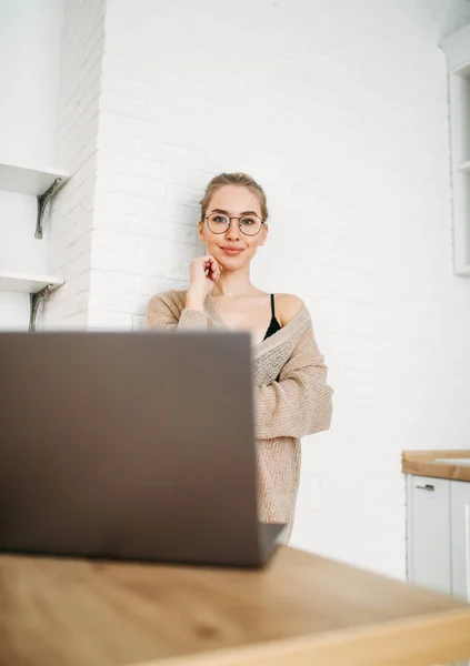 Schöne lächelnde junge Frau helles langes Haar Mädchen in Brille trägt in gemütlichen Strickpullover mit Laptop in heller Küche — Stockfoto