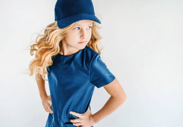Smiling curly hair tween girl in blue leather dress and baseball cap on the white background isolated — Stock Photo, Image
