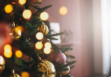 Altın ve mor oyuncaklarla süslenmiş Noel ağacı. Işıklar bokeh desenli.