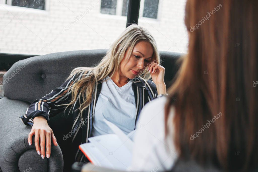 Upset young woman in office of psychotherapist or doctor, women communicate to each other, coaching or psychotherapy