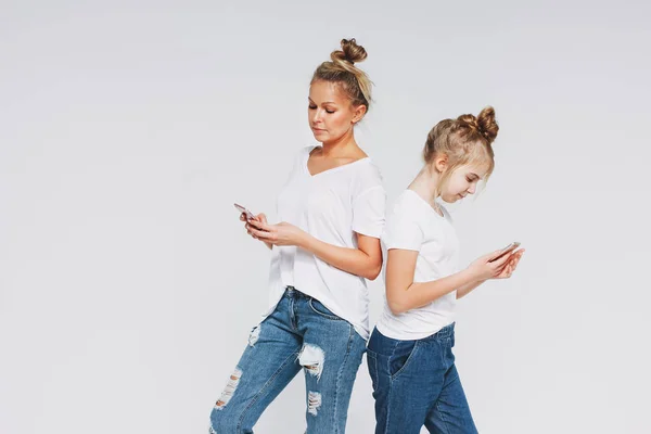 Blonde mom and daughter in white t-shirts and jeans using mobile phones gadgets concept isolated on white background — 스톡 사진