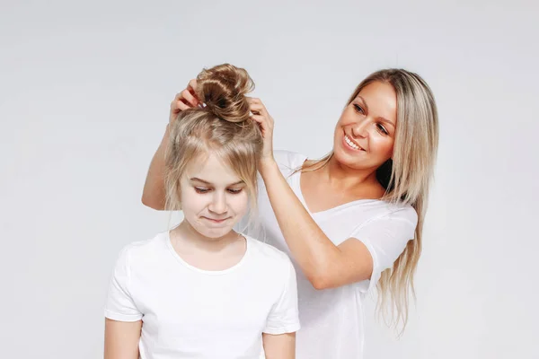 Young beautiful blonde woman make hair style for girl. Joint leisure of mother and daughter. Isolated on white background — Stock Photo, Image