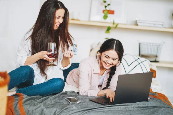 Jonge zorgeloze brunette meisjes in casual met glas wijn online kopen met kredietkaart op laptop, winkelen van thuis — Stockfoto