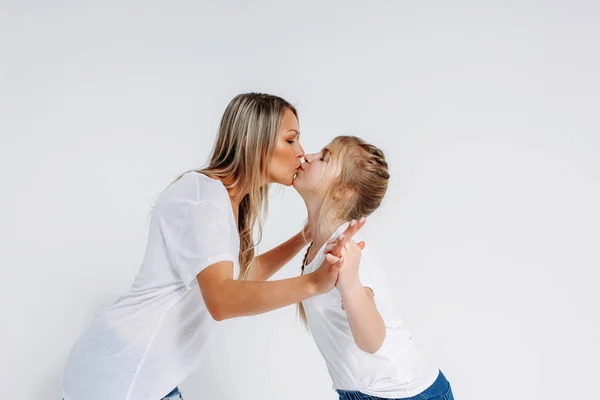 Real mãe e filha em camisetas brancas e jeans beijando isolado no fundo branco — Fotografia de Stock