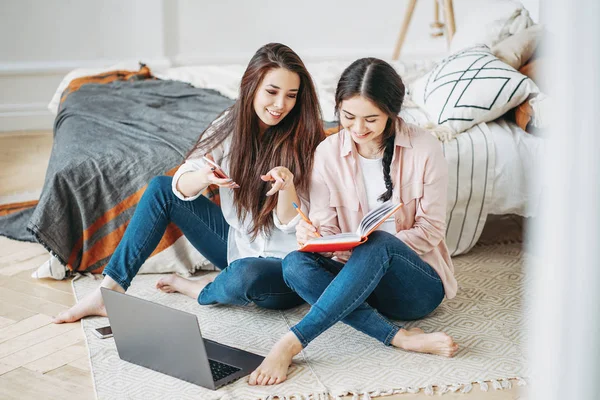 Jonge brunette meisjes vrienden studenten in casual doen project samen op zoek naar informatie in internet door mobiele en laptop op kamer — Stockfoto