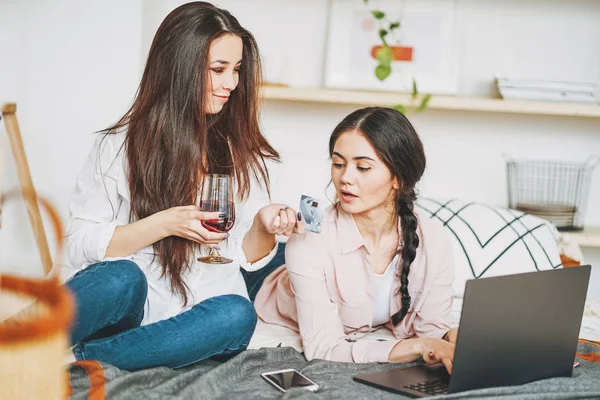 Jonge zorgeloze brunette meisjes vrienden in casual met glas wijn online kopen met creditcard op laptop, winkelen vanuit huis — Stockfoto