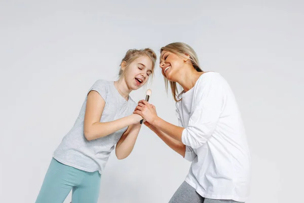 Young beautiful blonde mom and daughter in pajamas having fun together isolated on white background — Stock Photo, Image