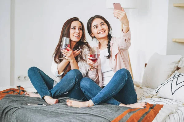 Jovens despreocupados morena meninas amigos casuais com copos de vinho tomando selfie e se divertindo juntos na festa em casa — Fotografia de Stock