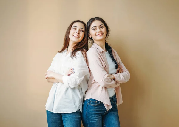 Młoda beztroska brunetka uśmiechnięta dziewczyny przyjaciele siostry w casual koszule i dżinsy izolowane na beżowym tle — Zdjęcie stockowe