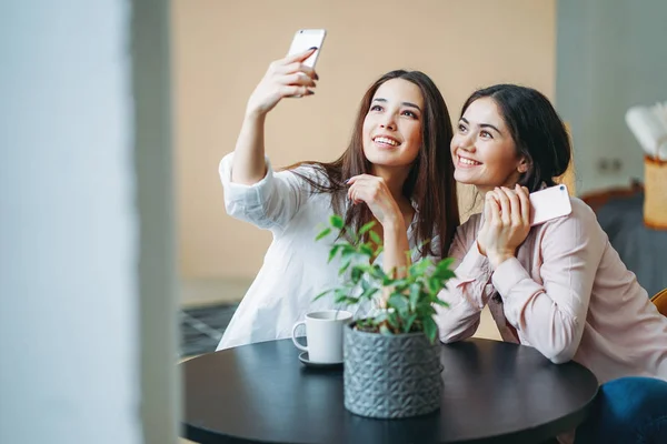 Fiatal gondtalan barna lányok barátok alkalmi mobiltelefonok csinál szelfi az asztalnál — Stock Fotó
