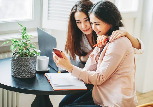 Jonge zorgeloze brunette meisjes vrienden studenten in casual met koppen van thee vergadering met gadgets op helder interieur — Stockfoto