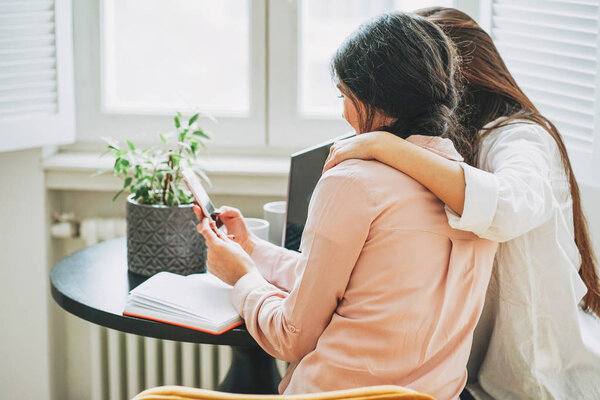 Young carefree brunette girls friends students in casual with gadgets at bright interior, view from behind