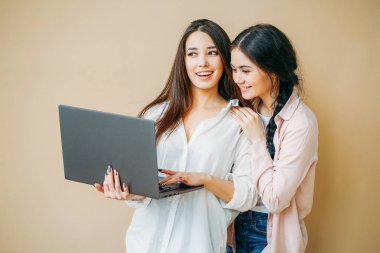 Young smiling girls students in casual with laptop in hands isolated on beige background