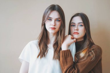 Genç, güzel, uzun saçlı kızlar bej arka planda günlük izole edilmiş ikizler.