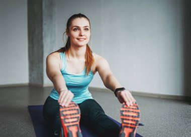 Çekici formalı genç bayan spor giyim fitness mankeni stüdyo çalışma sınıfında esneme hareketleri yapıyor.