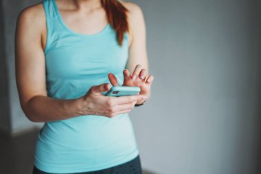 Çekici fit genç bayan açık mavi spor giysisi antreman sınıfında cep telefonuyla antrenman yapıyor.
