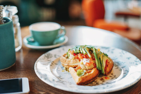 Vegetarian waffles with fresh vegetables and avocado business lunch coffee mobile phone white screen at table in the cafe