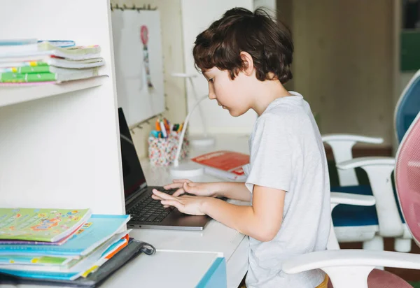 Tween boy do homework learn foreign language writing in pupil book with opened laptop at the room home dictance education