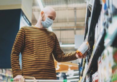 Tıbbi maskeli kel adam süpermarketten ürünler seçiyor. Coronavirus karantina konsepti.