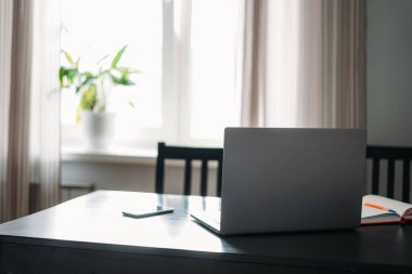 Siyah masada cep telefonu ve pencereye karşı notlarla açılan dizüstü bilgisayar. 