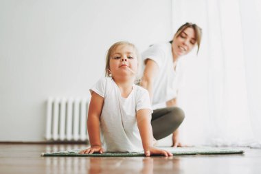 Mutlu anne ve küçük kızı birlikte yoga yapıyorlar. Parlak iç mekanda.