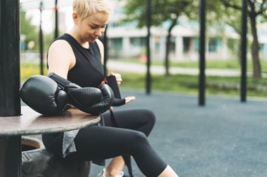 Sporcu kızın arka planında siyah deri boks eldivenleri antrenmandan önce ellerinde boks bandajları sallıyor.