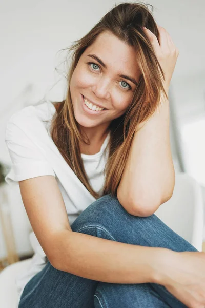 笑顔の若い女性の茶色の髪と白いTシャツとカメラを見てジーンズでそばかすと緑の目の肖像 — ストック写真