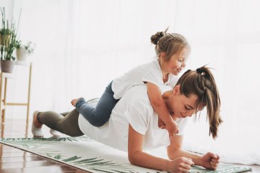 Mutlu anne ve küçük kızı birlikte yoga yapıyorlar. Parlak iç mekanda.