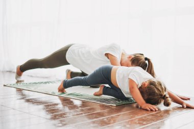 Mutlu anne ve küçük kızı birlikte yoga yapıyorlar. Parlak iç mekanda.