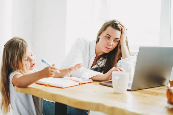 Dizüstü bilgisayarda serbest çalışan bir anne ve evde küçük bir kız çizim yapıyor.