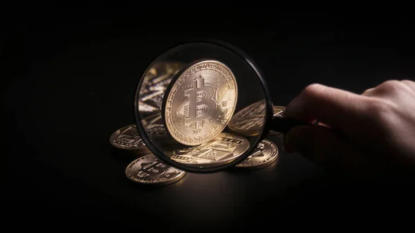 Unerkennbare Person hält Vergrößerungsglas in der Hand und blickt durch es auf neues virtuelles Geld goldene Bitcoin auf schwarzem Hintergrund platziert. — Stockbild Unerkennbare Person hält Vergrößerungsglas in der Hand und blickt durch es auf neues virtuelles Geld goldene Bitcoin auf schwarzem Hintergrund platziert. — Stockfoto
