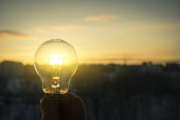hand holding a light bulb against the setting sun
