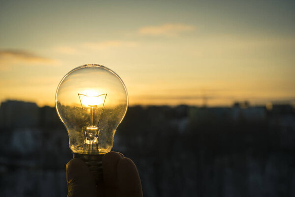 hand holding a light bulb against the setting sun