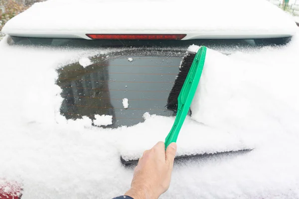 Man rengör bilen från snö med pensel. Snötäckt bilvindruta. parkerad bil täckt med snö under snö på vintern. — Stockfoto
