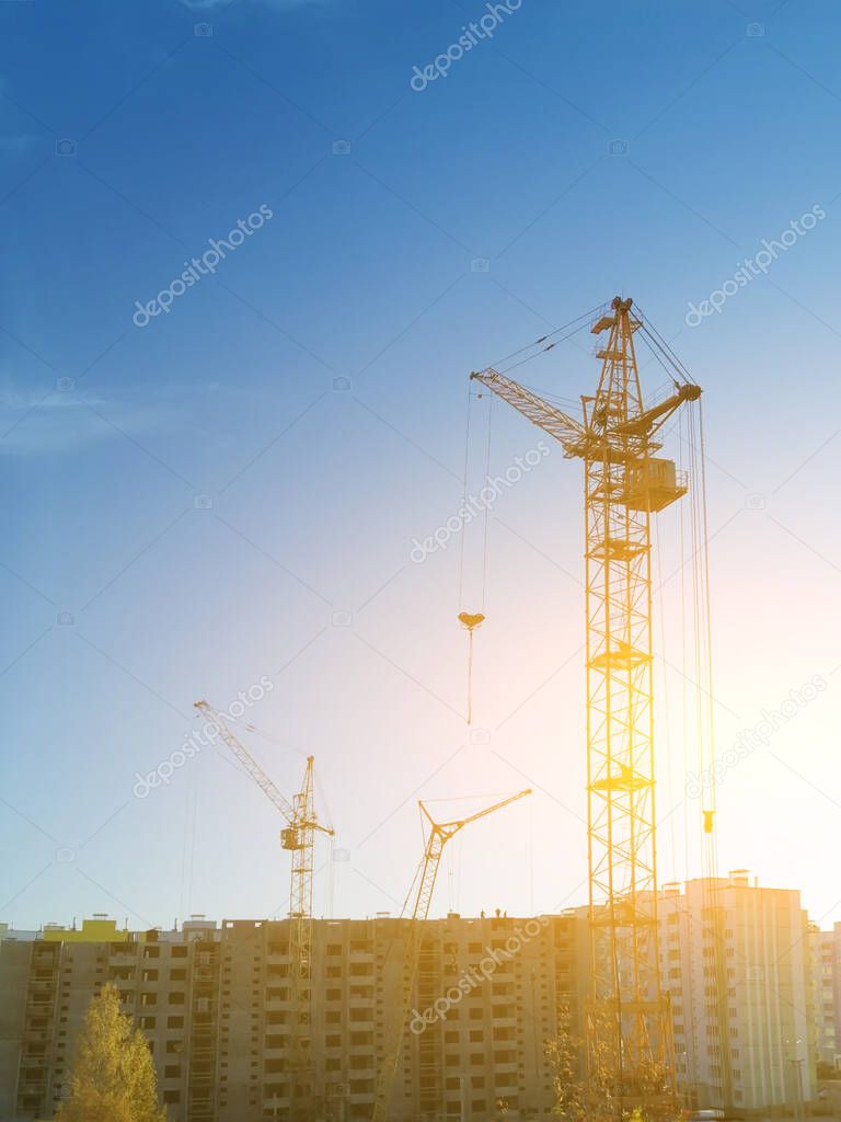 the construction crane and the building against the blue sky and sun