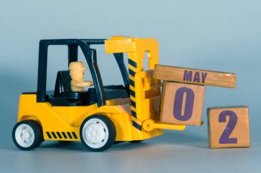2 Mayıs. Ayın ikinci günü, inşaat takvimi ya da depo takvimi. Sarı oyuncak forklift tahta küplere tarih yüklüyor. Çalışma planı ve zaman yönetimi. Bahar ayı, yılın günü konsepti.