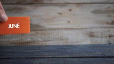 19 Haziran 'da. Ayın 19 'u, renk küpleri takvimi. El, ayın gününü ayın adına tahtadan bir arka plana koyar. Yaz, yılın günü konsepti.