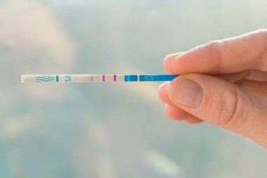 Bulanık arka planda kadın eliyle yapılan hamilelik testi. Pozitif bir hamilelik testi tutan kadın eli yakın plan..