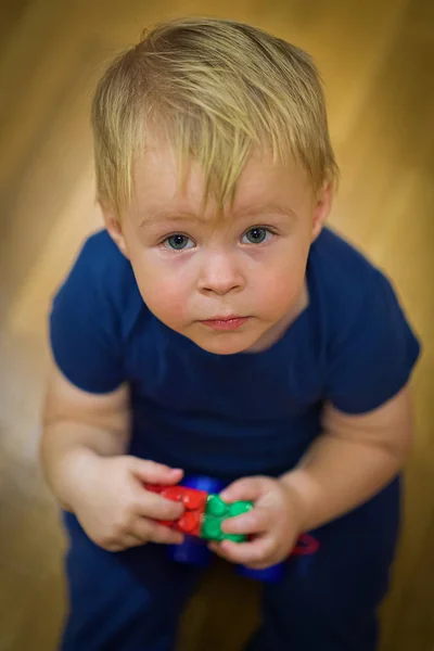 Portrait d'un petit garçon mignon avec des jouets dans ses mains assis sur le sol, levant les yeux. vue de dessus — Photo