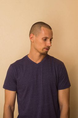 Mavi tişörtlü çekici bir genç bej bir duvara karşı poz veriyor..