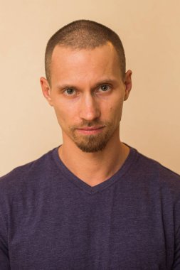 Düşüncelere dalmış genç bir adamın portresi mavi ya da mor bir fotoball ile bej bir duvara yaslanmış.