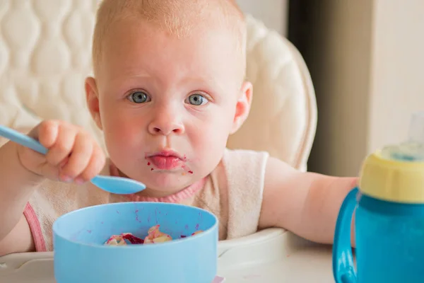 Мальчик учится есть. милый грязный ребенок ест овощи с ложкой самостоятельно в высокий детский стульчик — стоковое фото