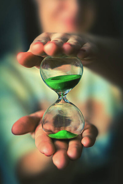 woman is holding hourglass in his hand. Life time passing concept. Sand running through the bulbs of an hourglass measuring the passing time in a countdown to a deadline