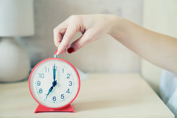 Closeup of woman hand reaching to turn off classic red alarm clock